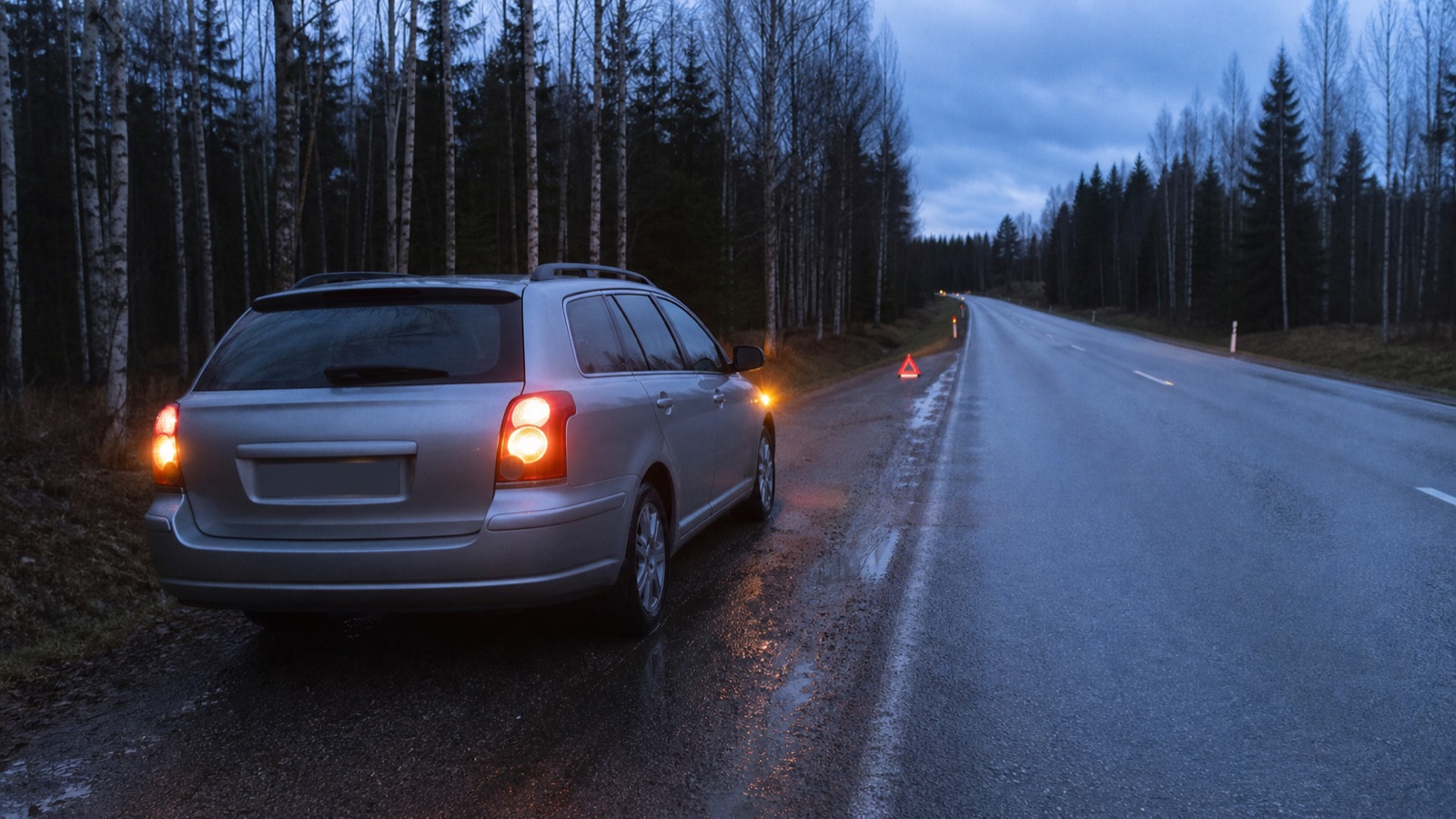 Auto hätävilkut päällä märän maantien pientareella ja varoituskolmio kauempana